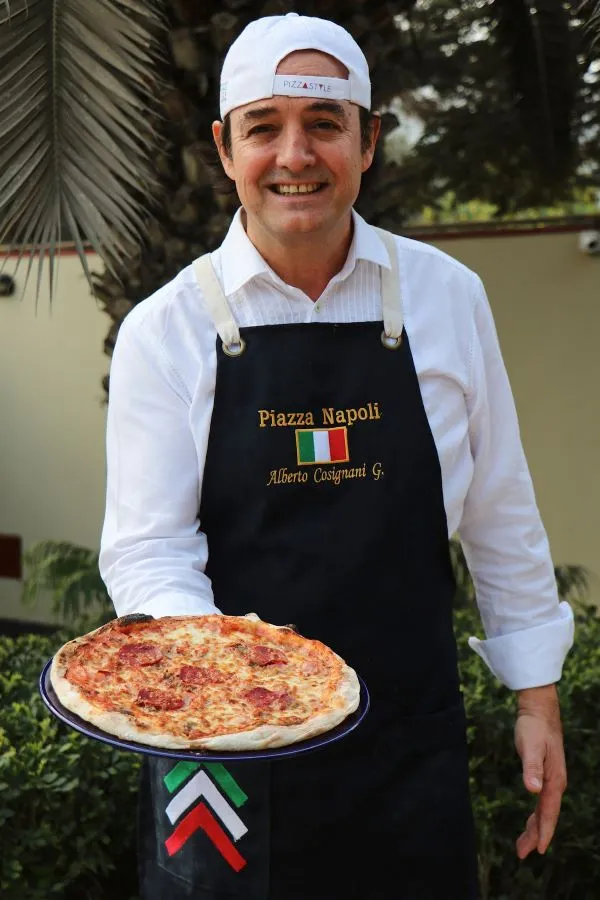 Pizzaiolo uniformado con pizza napoletana en la mano recién horneada